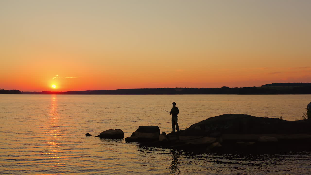 People fishing in the evening. Fishermen stand on a big stone surrounded by water at sunset. Silhouette of men with fishing rods against the setting sun.
