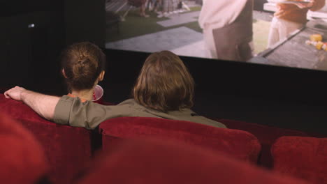 rear view of couple hugging sitting in the cinema while they watching a movie and talking 2