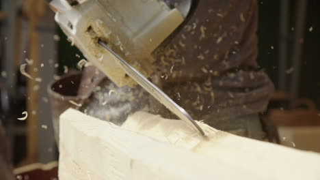 close-up of craftsman using chainsaw power tool to carve out wooden log