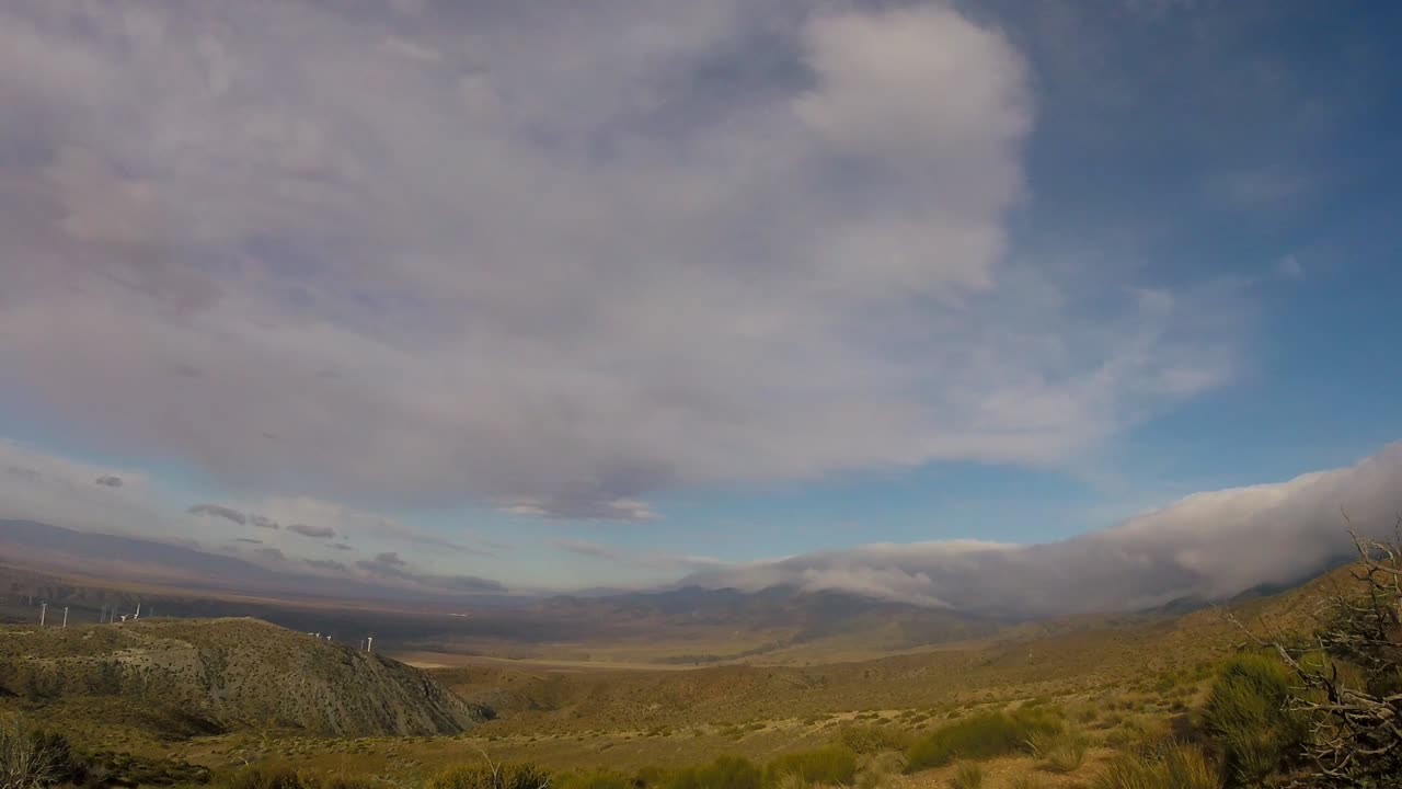lapso de tiempo de nubes tratando de soplar en el suelo del desierto con turbinas eólicas debajo