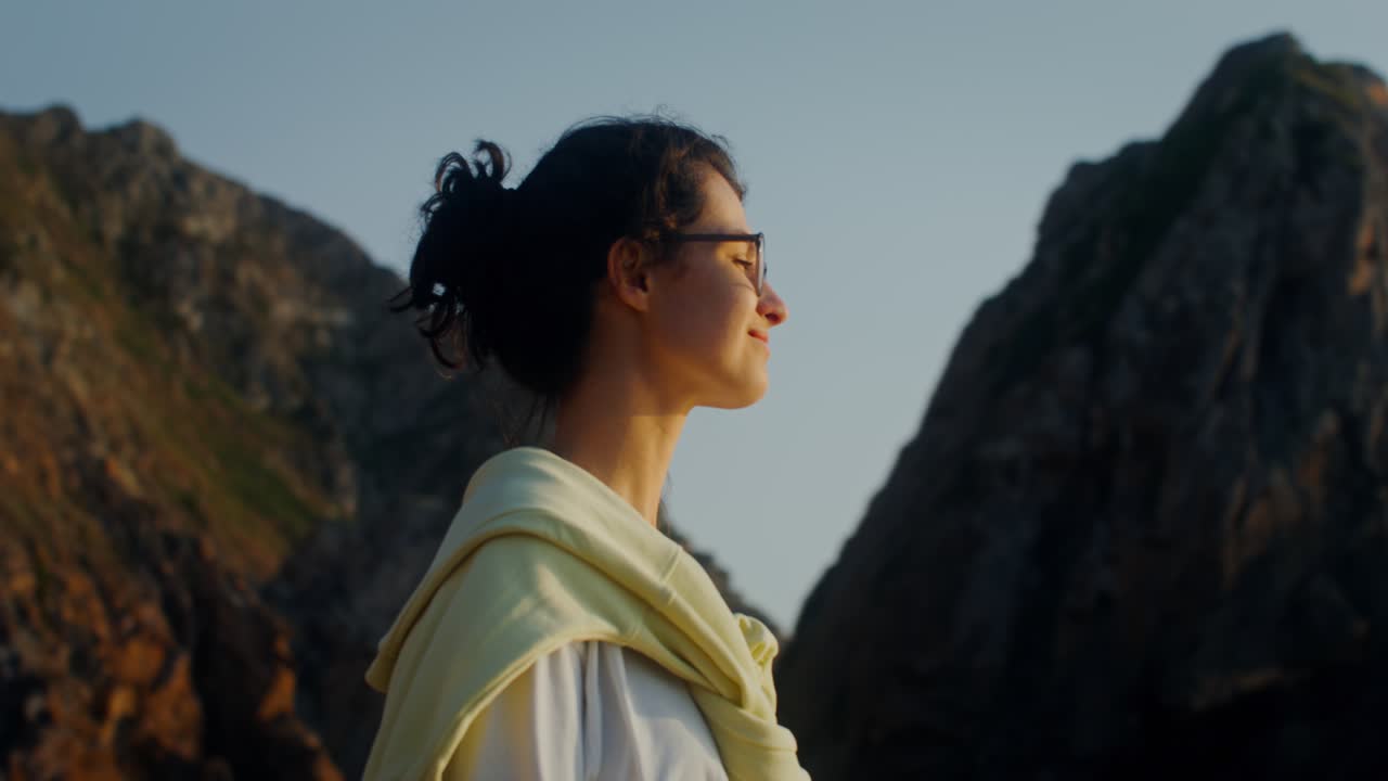 una mujer disfrutando de la puesta de sol junto a las rocas.