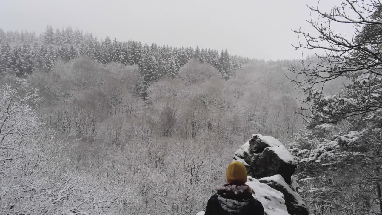 절벽 가장자리에 서있는 사람은 벨기에 하이 펜스에서 겨울 동안 눈으로 덮인 숲이 있는 길과 계곡을 보여줍니다.