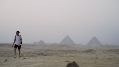 young egyptian man walks in desert with giza pyramids in distance, slow motion