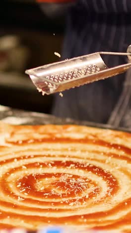 Chef grates cheese over pizza dough