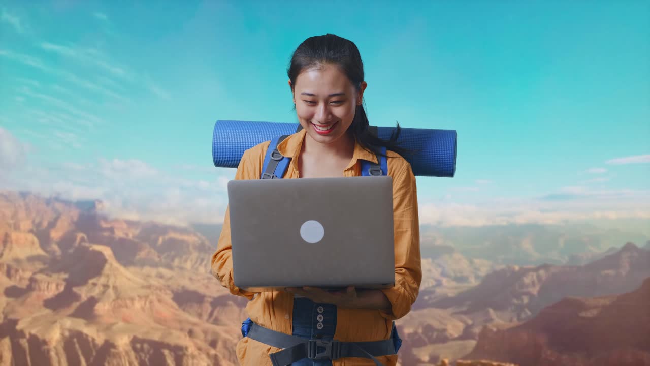 Asian Female Hiker With Mountaineering Backpack Using A Laptop While Traveling At The Top Of Mountain