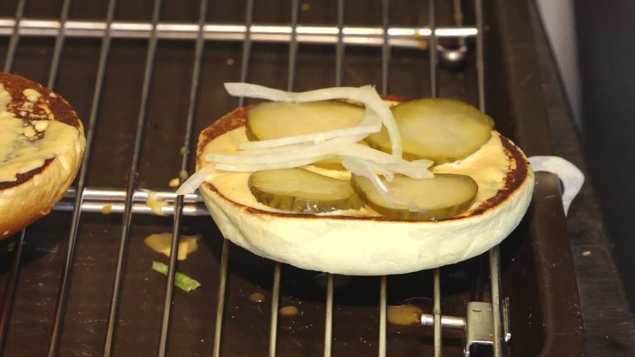 Primo piano di un doppio cheeseburger di manzo in fase di assemblaggio su una griglia, con formaggio fuso, lattuga sminuzzata e pane tostato