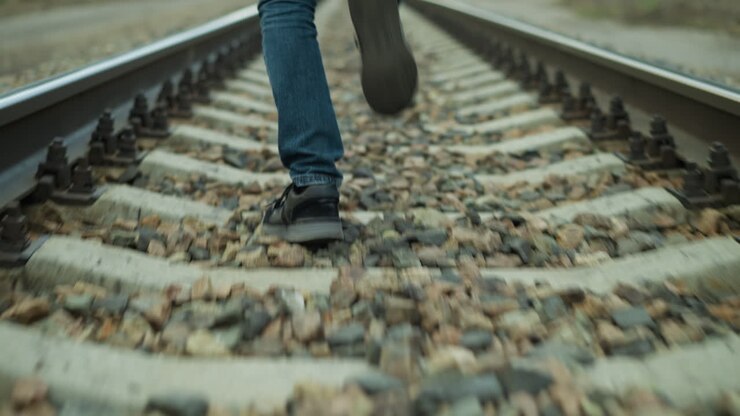 A close view of someone running on a railway track, wearing jeans and canvas shoes, the track is covered with stones