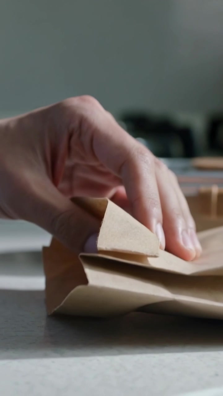 Vertical video: Folding hands tucking brown bag on kitchen counter, inserting white item for lunch