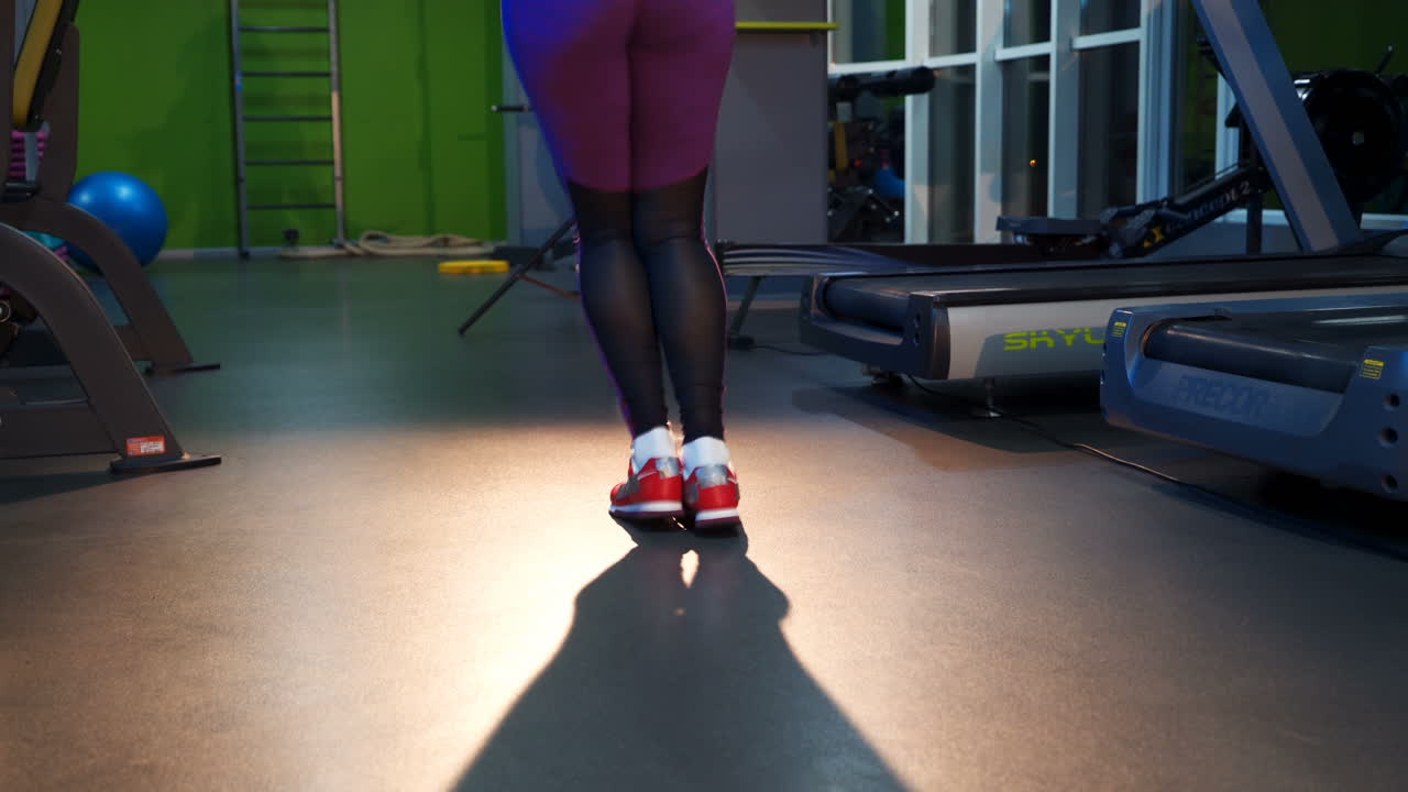 Back view of woman's legs in athletic leggings and comfortable sport outfit jumping rope on a sport club. Fitness female doing skipping workout