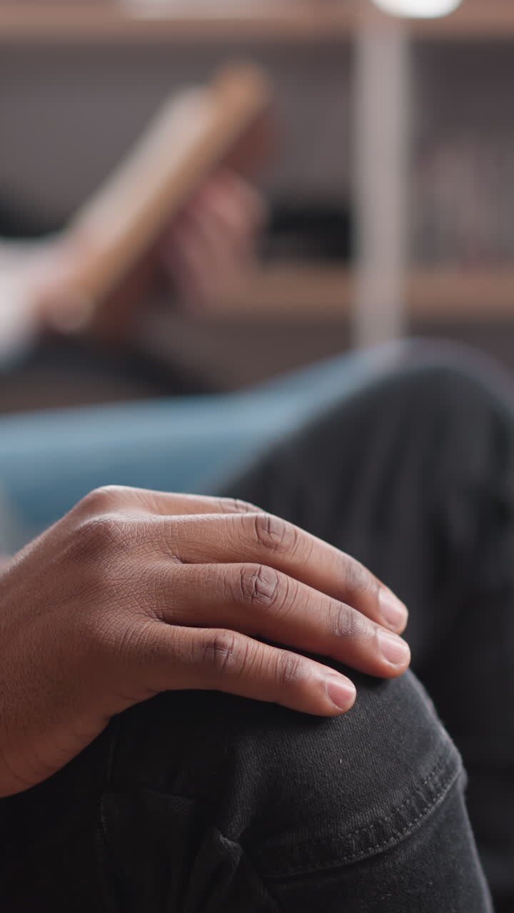 Black man taps fingers on knee indoors closeup. African American guy listens to rhythmical music with friends in chill out corner. Rest and relaxation