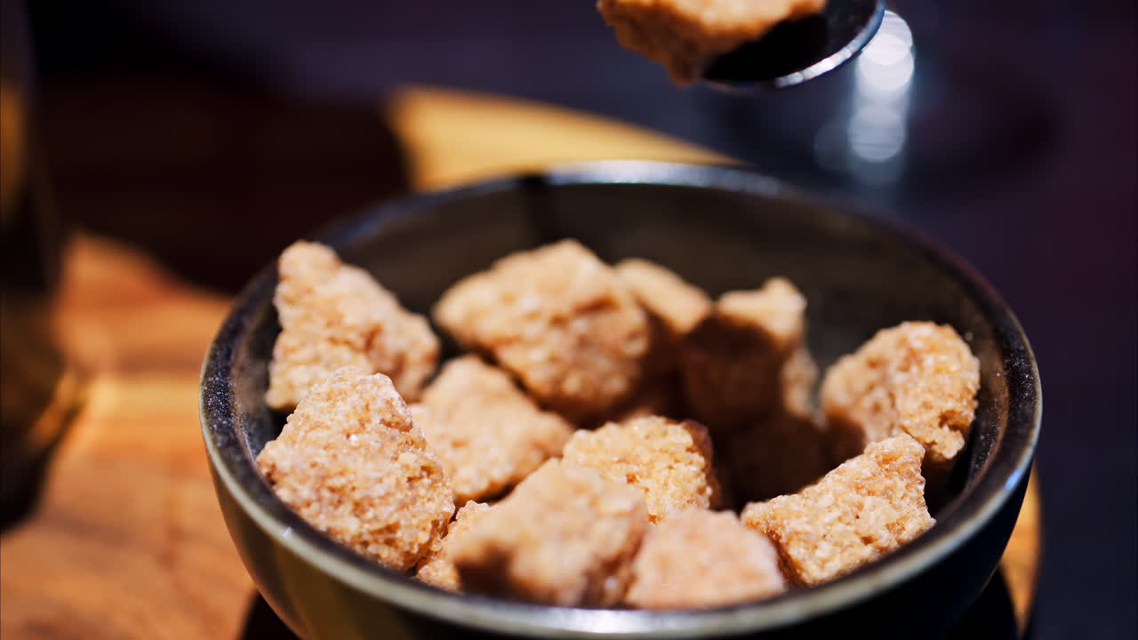 Close up of a spoon picking up brown sugar cubes from a black bowl