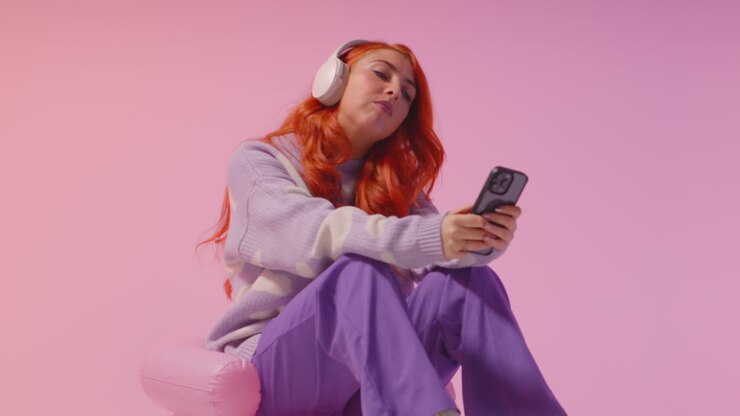 Scatto in studio di giovane donna della Gen Z con cuffie che ascolta musica in streaming dal cellulare 2