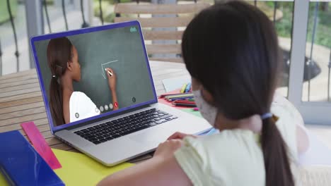 Kaukasisches-Schulmädchen-Mit-Gesichtsmaske,-Das-Einen-Laptop-Bei-Einem-Videoanruf-Mit-Einer-Lehrerin-Benutzt