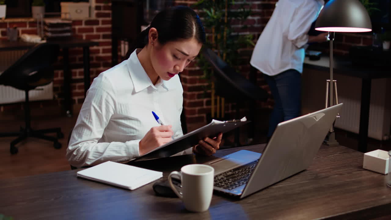 Businesswoman crosschecking data between laptop and paperwork