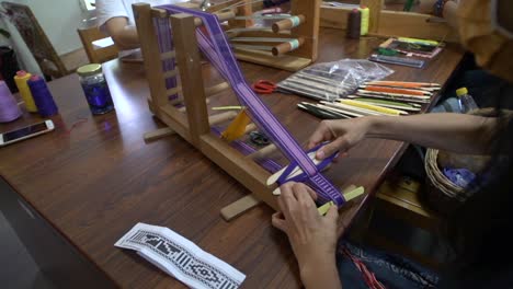 purple and white yarn being pressed and fitted using traditional asian weaving methods, filmed over shoulder as close up