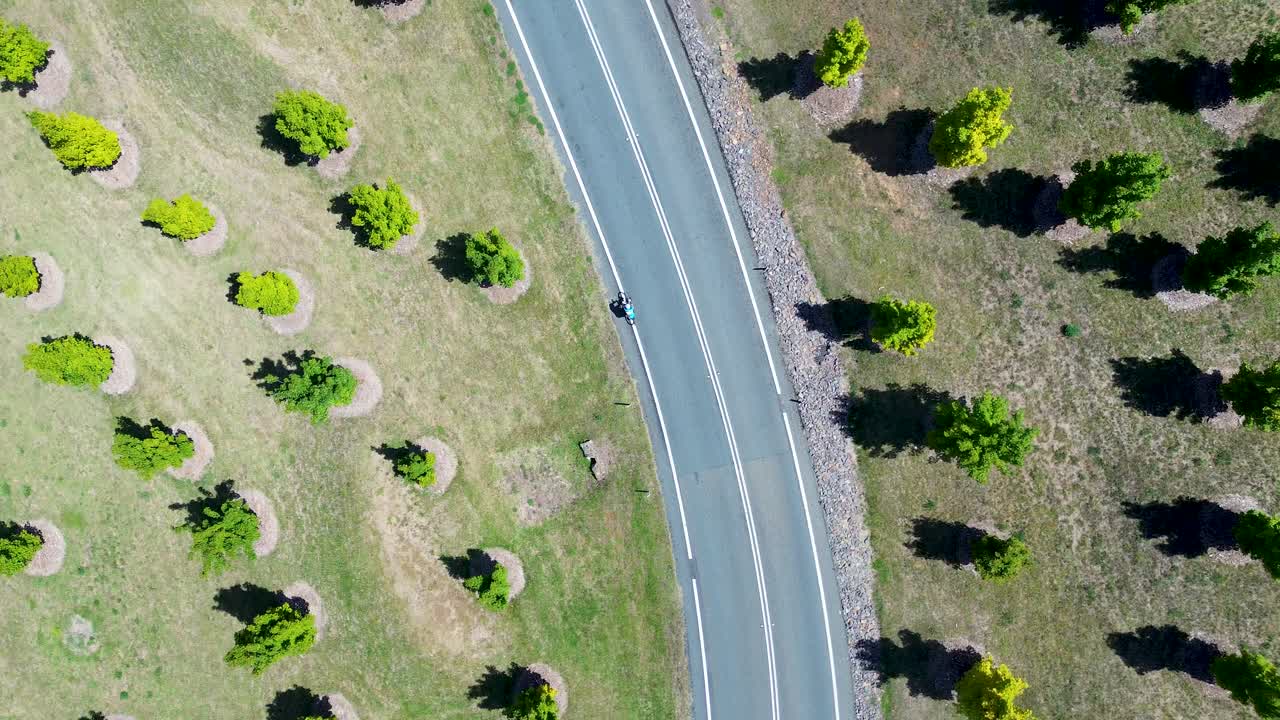 Drone aerial landscape of person on bike cycling uphill bend on road rural town street with trees vegetation National Arboretum Canberra ACT Australia leisure sports bicycle recreation exercise