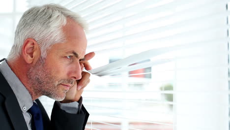 Businessman-spying-through-blinds-and-reporting-a-crime-on-his-phone