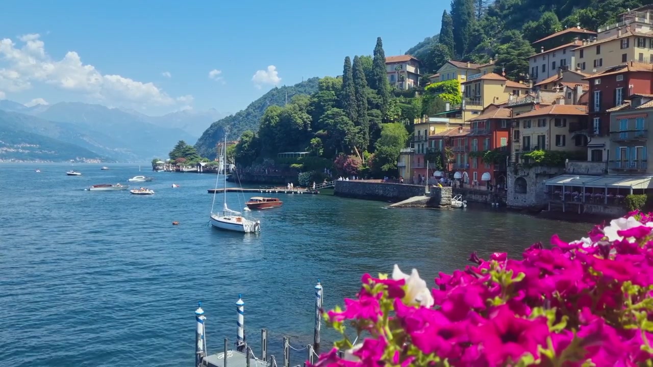 Pittoresca vista estiva del Lago di Como e Varenna, Italia, con piccole barche ancorate in calme acque alpine. Una destinazione di viaggio panoramica caratterizzata da cieli azzurri, fascino lacustre, nella rinomata località turistica italiana
