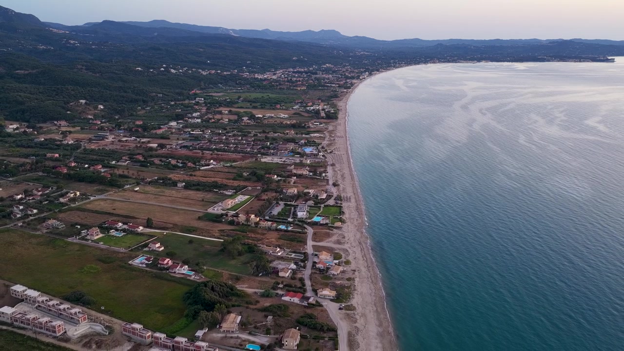 Una splendida ripresa aerea con drone ad alta quota che cattura l'ampia costa sabbiosa, il tranquillo Mar Ionio e gli sviluppi balneari di Almyros e Acharavi sull'isola di Corfù, Grecia, durante una serata tranquilla.