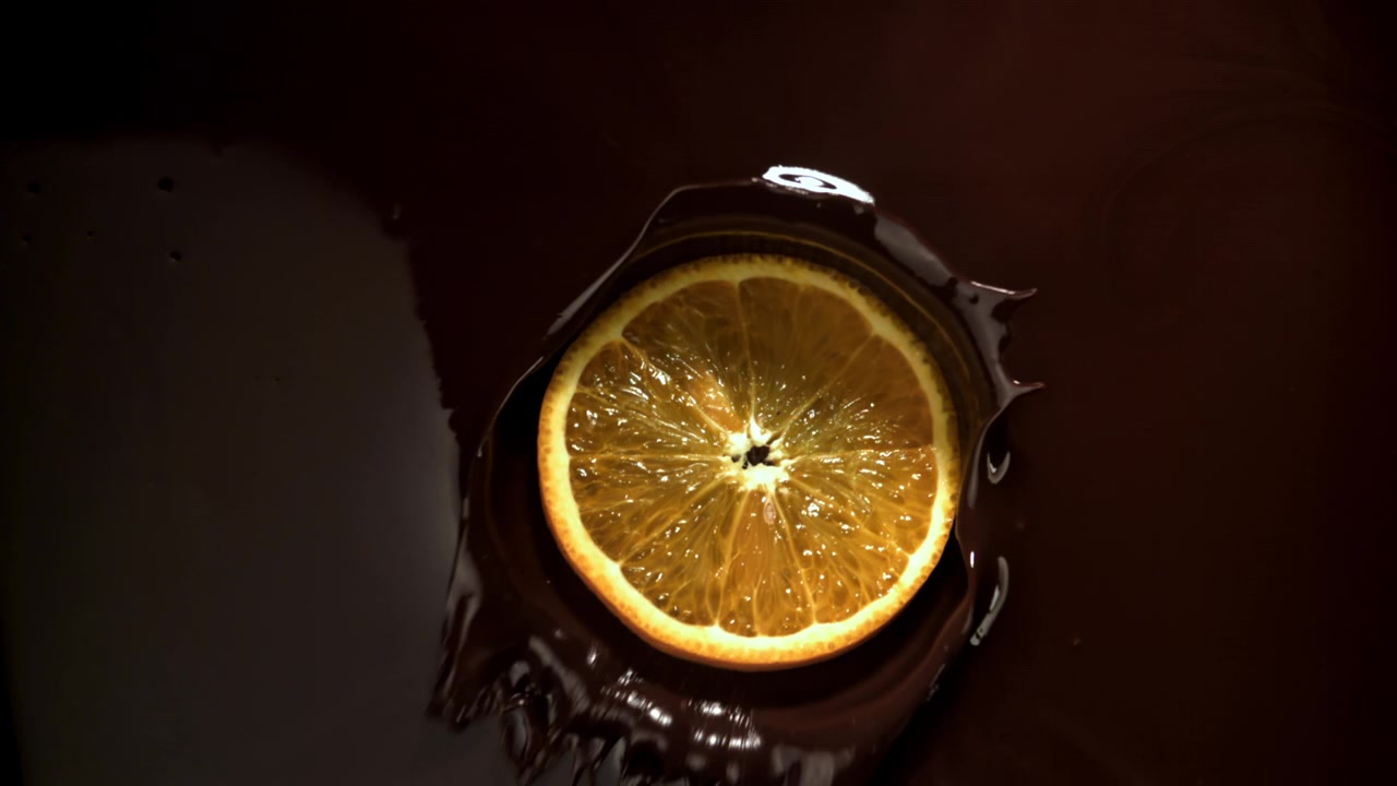 Fetta d'arancia che cade nel cioccolato fondente fuso