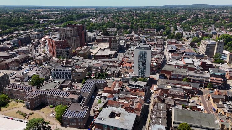 Wide view over the rooftops of a commuter town centre with a residential tower, car parks and shopping streets, with open countryside beyond