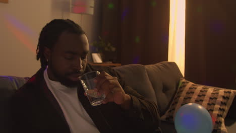 man sitting on sofa after drinking alcohol at house party drinking glass of water for hangover 2