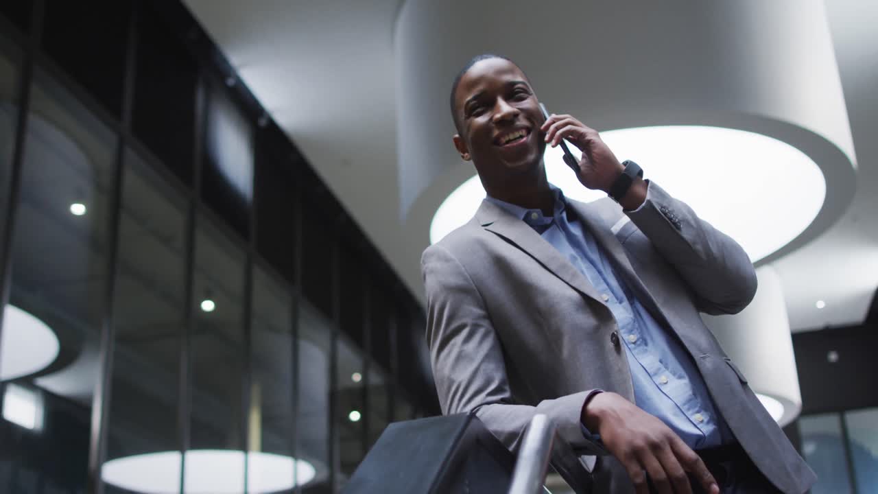 Afroamerikansk forretningsmand bruger smartphone i lobbyen af moderne kontorbygning