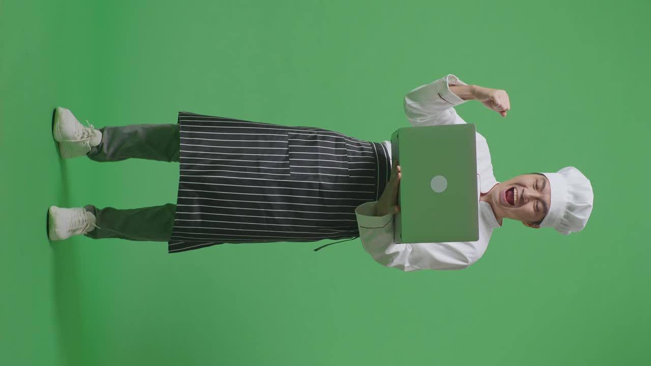 Full Body Of Asian Man Chef Looking At A Laptop Then Screaming Goal Celebrating While Standing In The Green Screen Background Studio