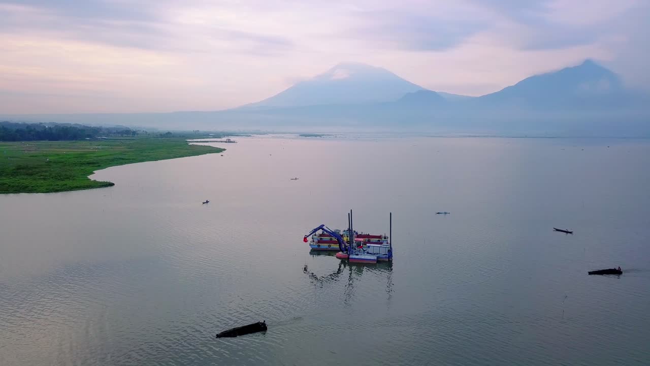 toma de drones de un bote dragador con excavadora en el lago con vista a la montaña en el fondo - lago rawa pening, indonesia