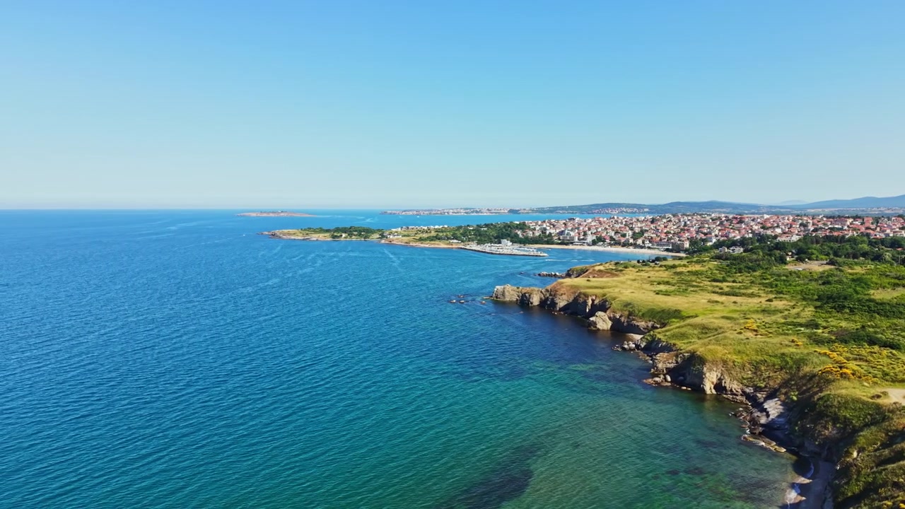 Vista della costa con acqua blu, terra verde e una città in lontananza in una giornata limpida, vicino alla riva.