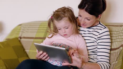 mother and daughter using tablet on couch