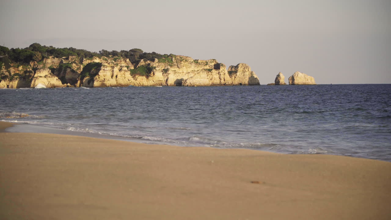 las olas rompen en la playa con los acantilados de alvor, portugal en el fondo