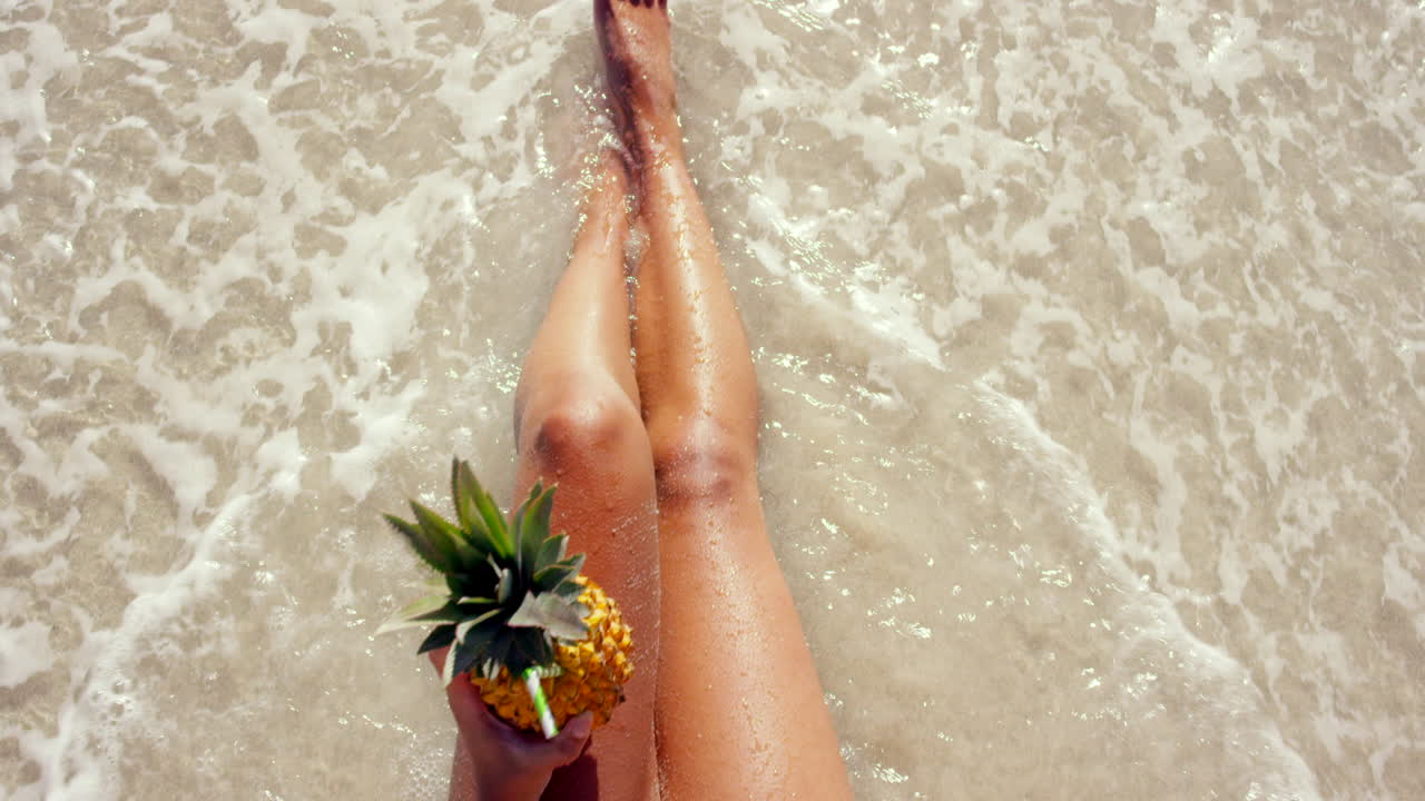 Kvinde slapper af på stranden med en ananasdrink