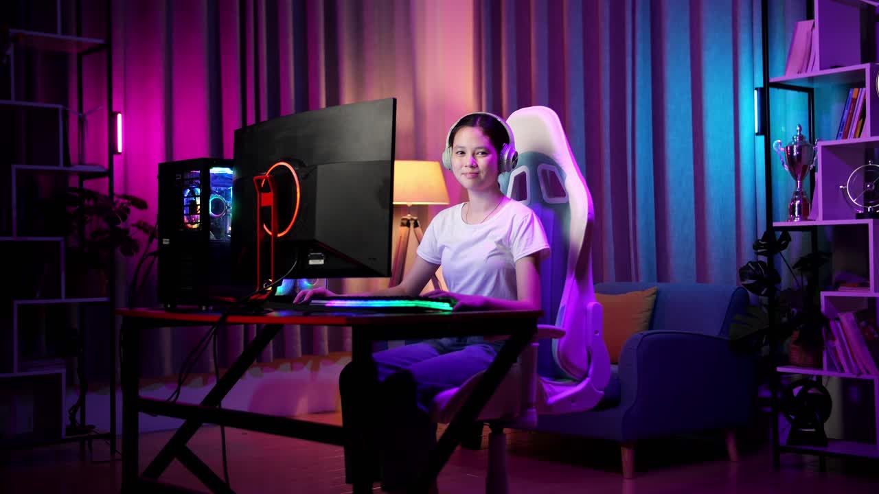 una adolescente asiática sonriendo a la cámara mientras juega videojuegos en la computadora
