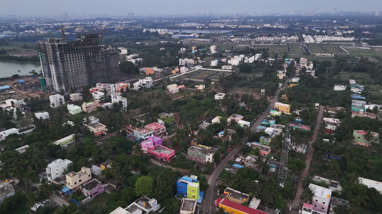 Filmato aereo di una città in rapida crescita. La vista include una varietà di architetture residenziali, da un quartiere tradizionale a un grande grattacielo incompiuto, il tutto situato vicino a un ampio lago.