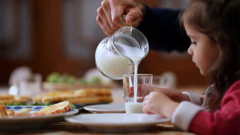 a person pouring milk into a glass for a child during a meal