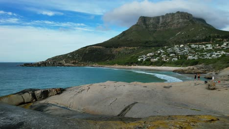 Wellen-Krachen-über-Große-Felsbrocken-Am-Strand-Von-Llandudno-Und-Der-Tafelberg-Im-Hintergrund,-Luftaufnahme