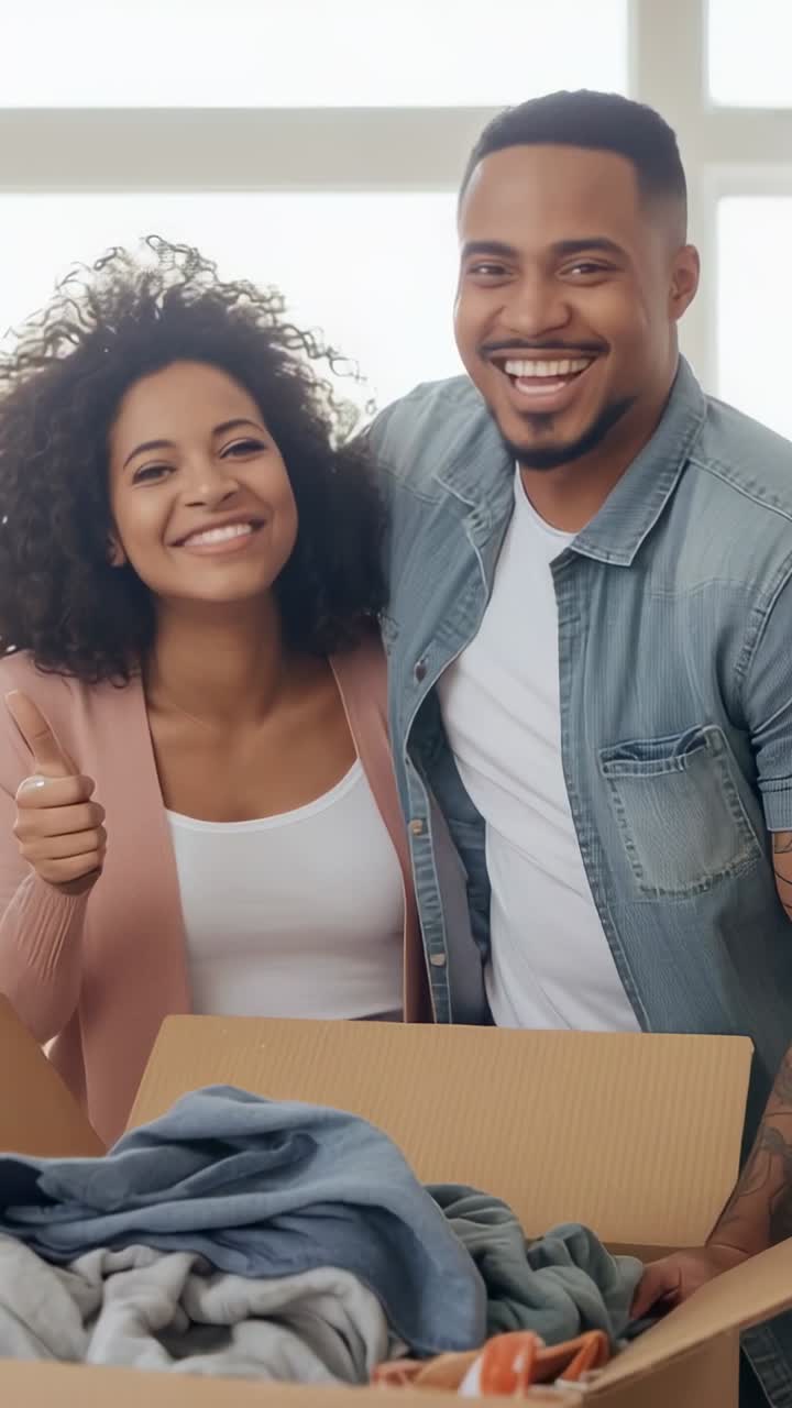 Vertical video: Slow zoom sparking smiling couple giving thumbs-up over clothes box in living area