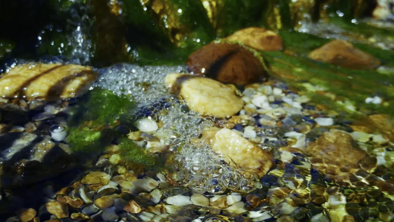Moss and glowing stones under running stream water in daylight.