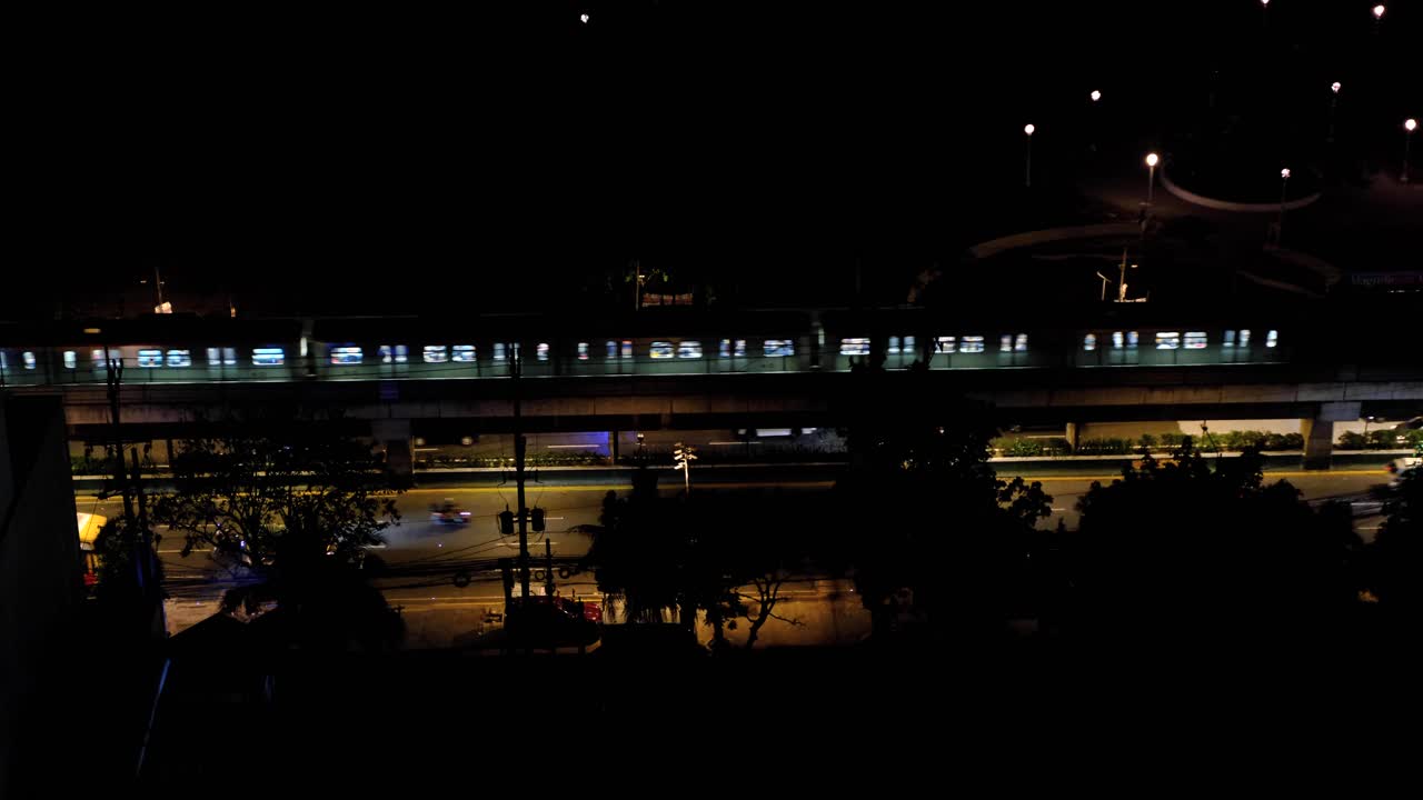 Aerial view of public transport train and traffic on highway with lights at night in capital city of Manila Philippines