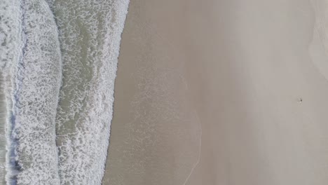 vertical shot foamy waves rushing into sandy shore of palm beach in gold coast, qld australia