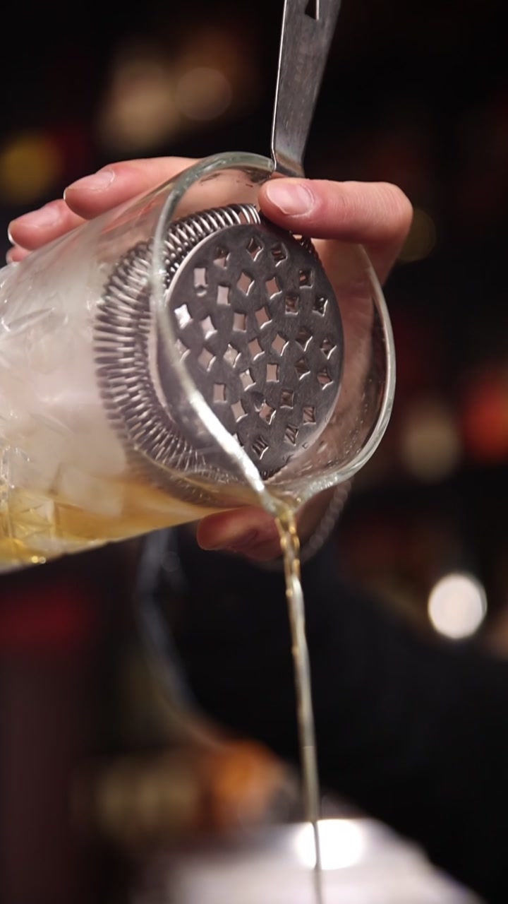 Barman professionista che filtra un cocktail da un mixing glass