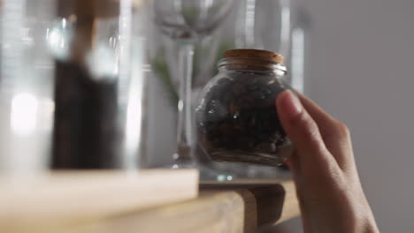 lady takes coffee from shelf in kitchen. woman reaches for glass jar filled with aromatic coffee beans on wooden shelf. hot beverage preparation