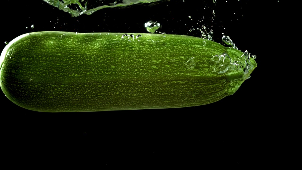 Zucchina verde fresca che si immerge nell'acqua, creando bolle.