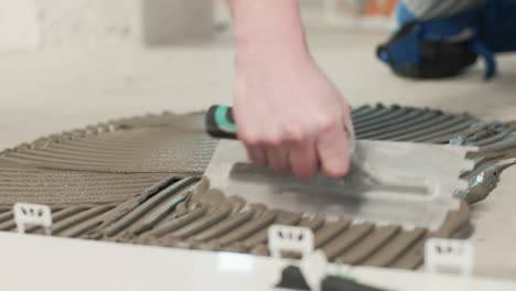 construction worker spreading tile adhesive on the cement floor for placing tiles