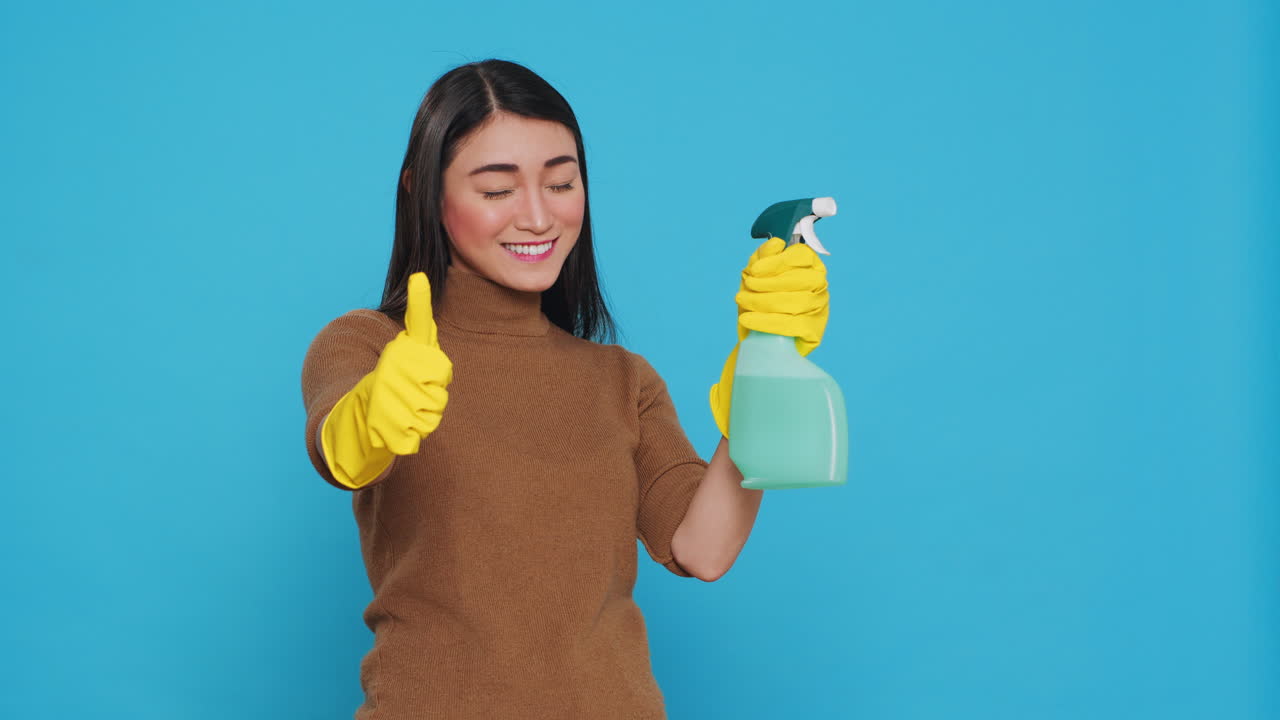 Smiling positive housekeeper holding chemical detergent spray doing approval gesture
