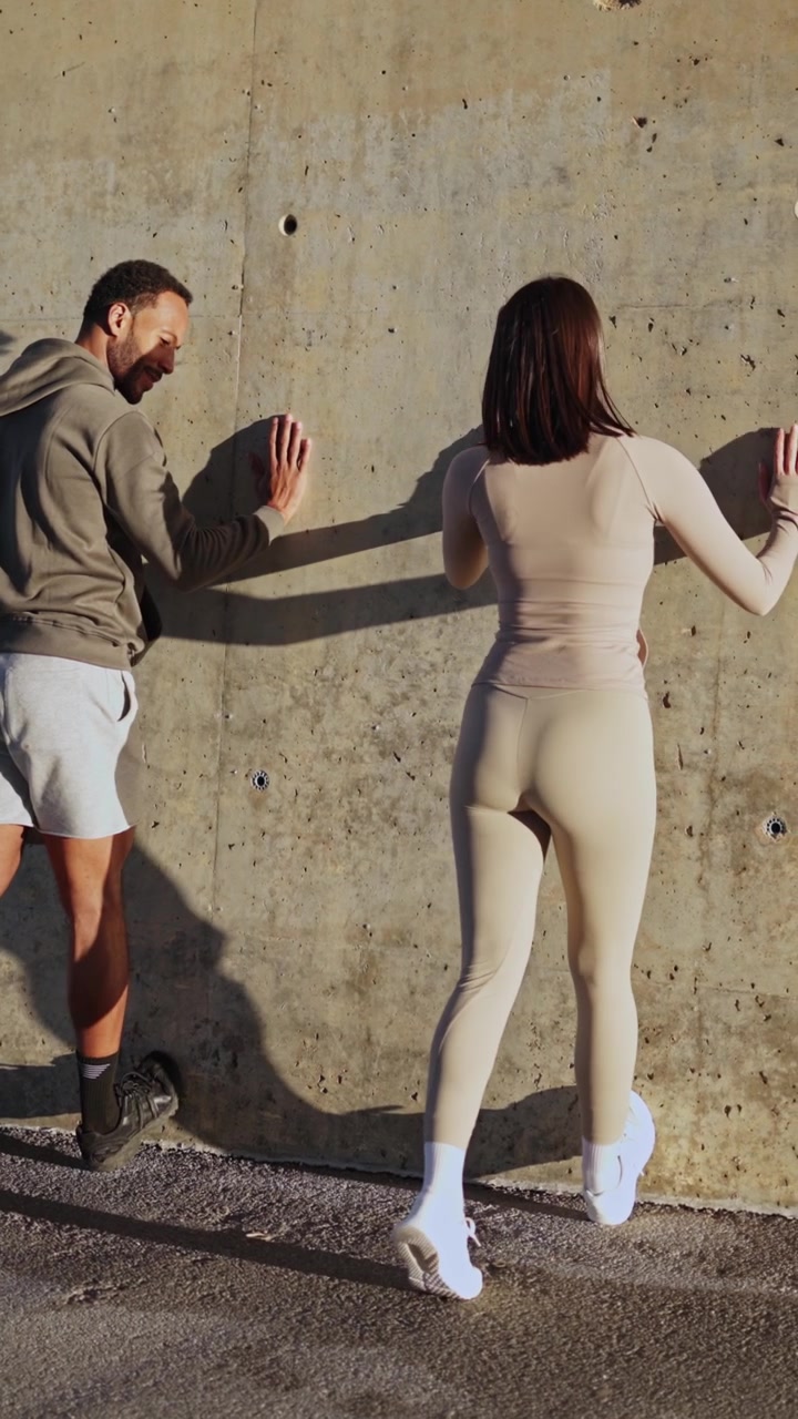 Personal trainer che assiste una donna con un esercizio di stretching al muro