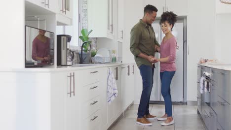 Happy-african-american-couple-dancing-and-holding-hands-in-kitchen