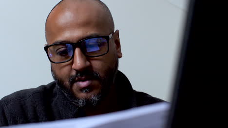 primer plano de un hombre con gafas, que parece ansioso y desanimado mientras lee documentos, posiblemente relacionados con las facturas o el costo de la vida