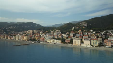 Stunning-orbiting-aerial-view-of-the-quaint-coastal-Italian-village-town-of-Varazze,-Liguria-with-calm-waters-and-mountainous-background